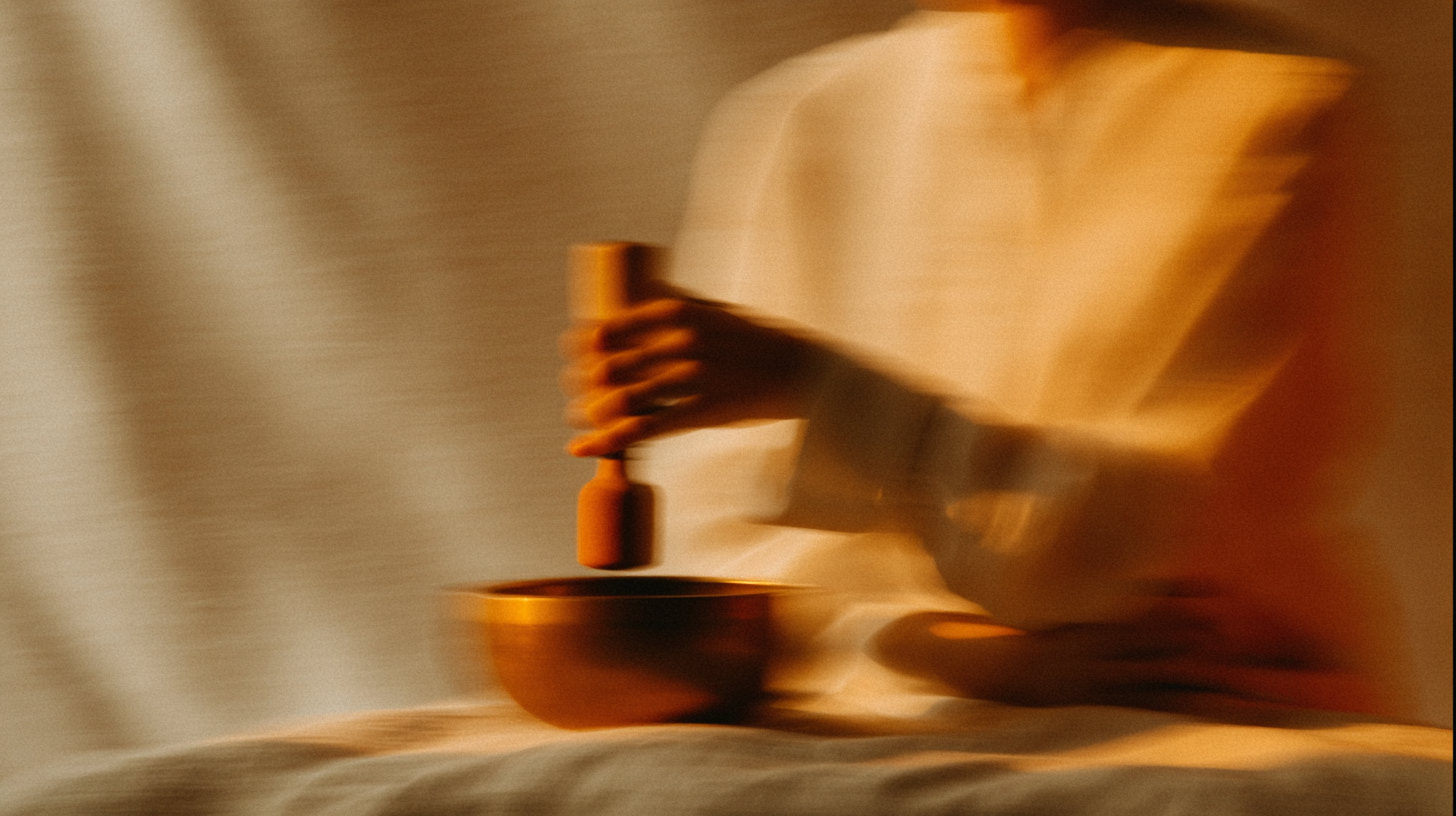 Person in a light robe using a  wooden mallet with a singing bowl on a soft fabric surface, symbolizing holistic wellness and mindfulness rituals